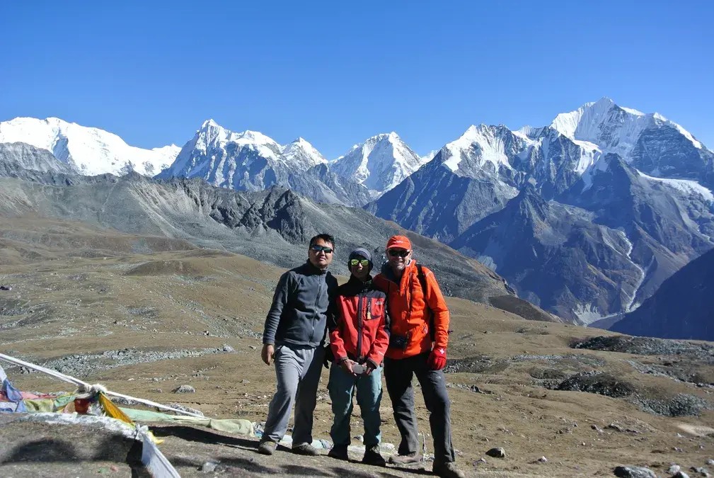 Trekkers wearing fleece layers, windproof jackets, and strong hiking boots posing with the snow-covered Langtang mountain ranges in the background.