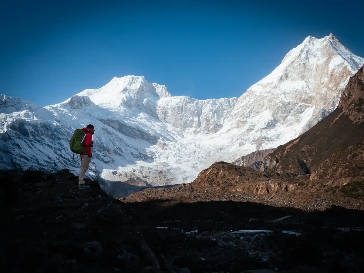 Nepali trekking guide performing a traditional prayer gesture in front of Mount Manaslu with clear blue sky and Himalayan landscape