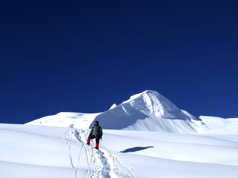 Experienced guide climbing Mera Peak with snow-covered slopes and Himalayan mountains in the background, Nepal.