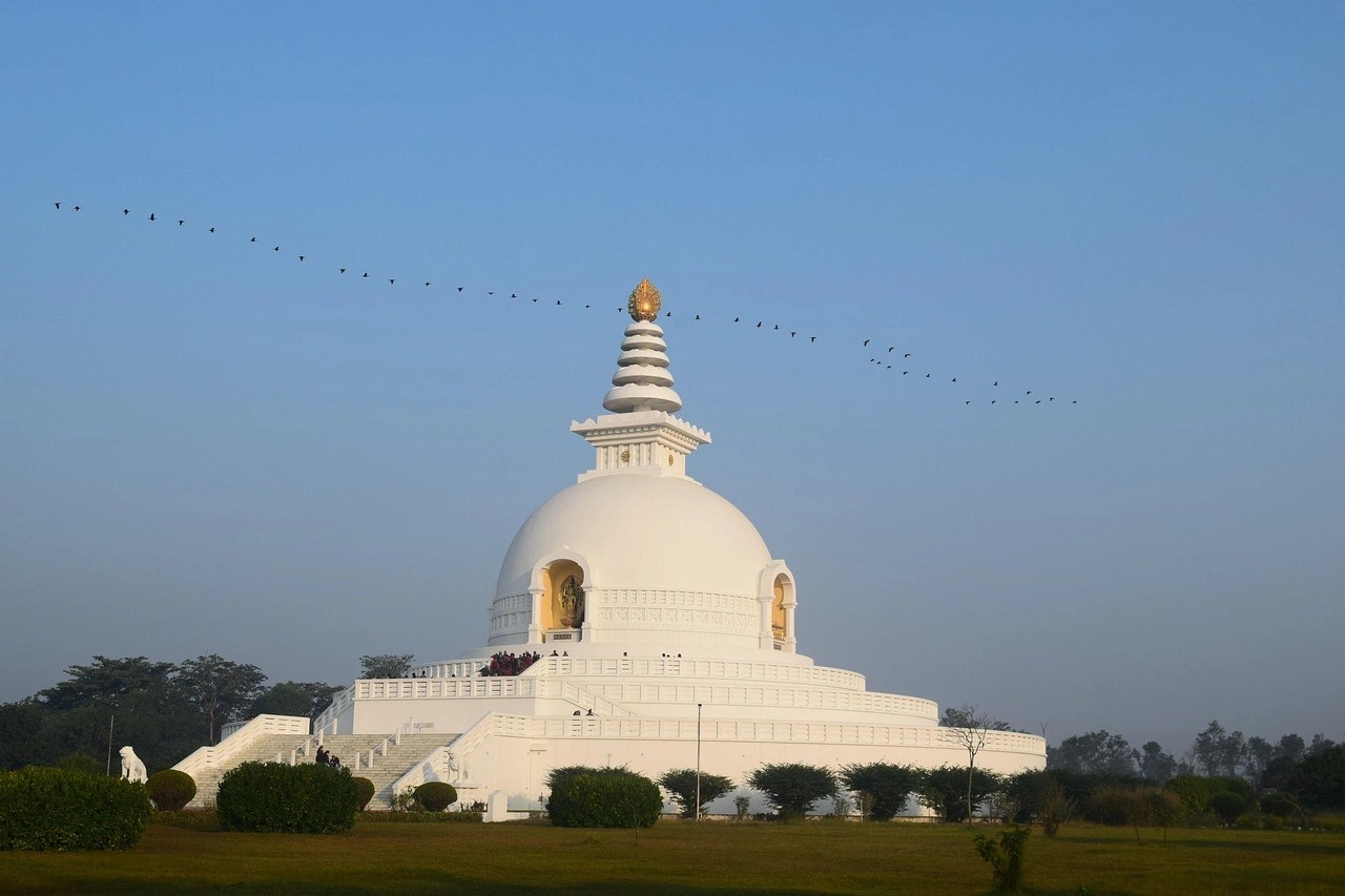 Lumbini Peace Pagoda in Nepal with serene gardens, water reflections, and a clear sky background.