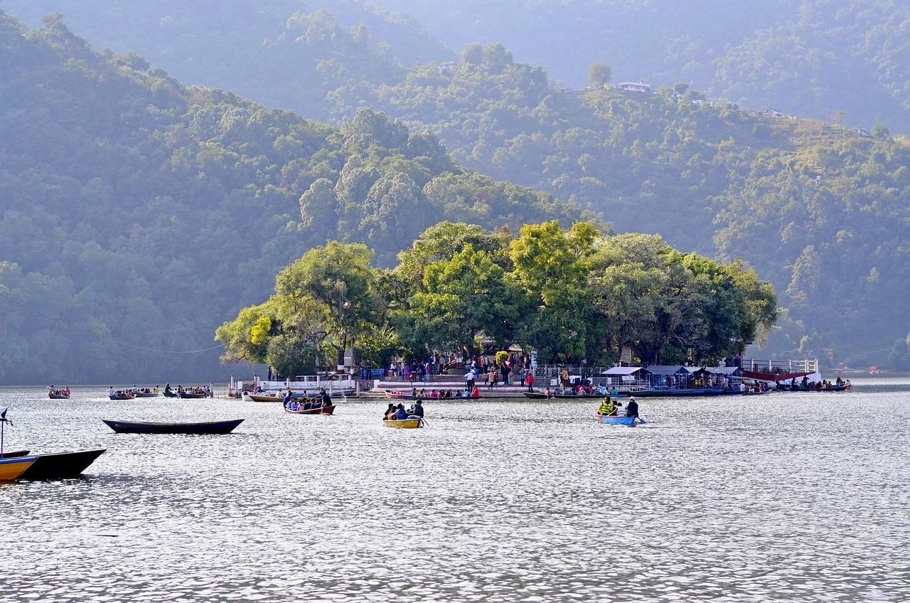 Boats on Phewa Lake in Pokhara with Tal Barahi Temple in the center of the lake and mountains in the background.
