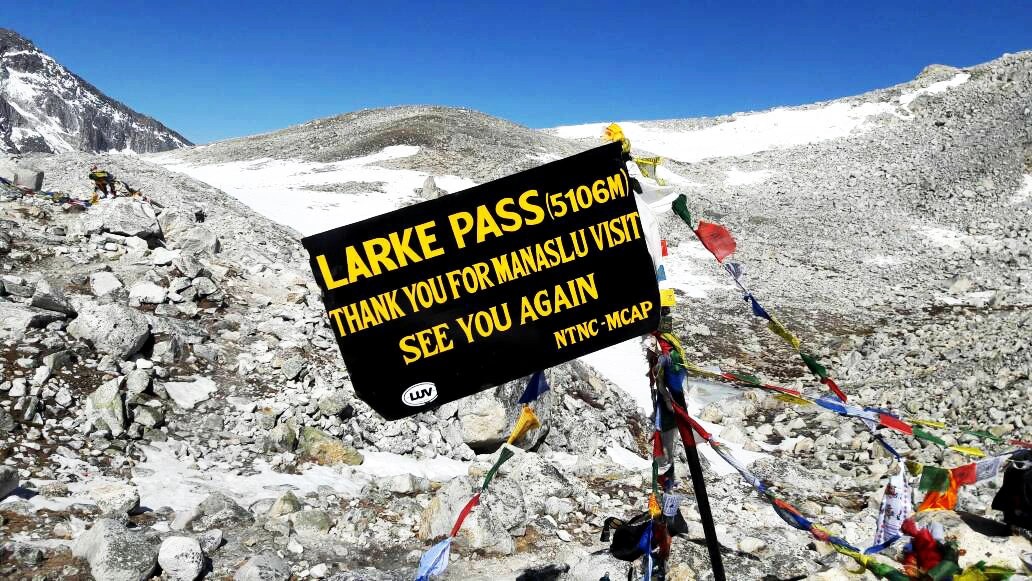 Larkya La Pass signboard at high altitude in Manaslu Circuit Nepal with snowy mountains in background.