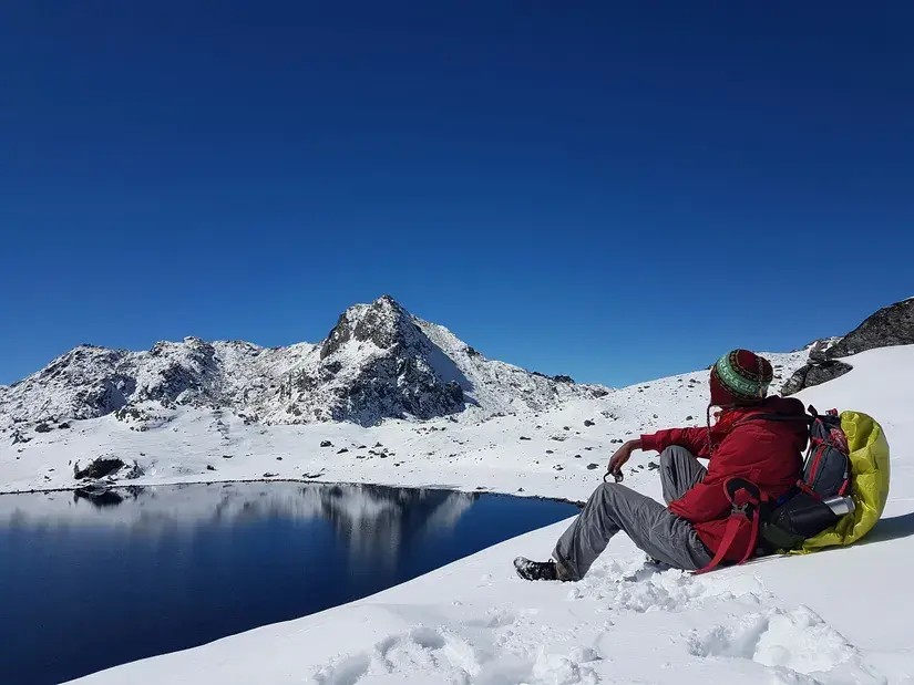 Trekking guide standing quietly beside Gosaikunda Lake with clear alpine water and rugged Himalayan mountains in the background.