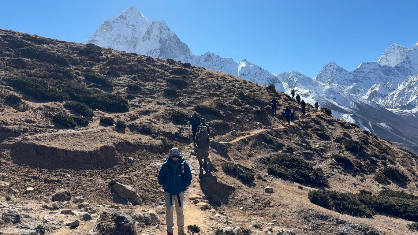 Trekkers walking toward Everest Base Camp with Ama Dablam rising behind the trail.