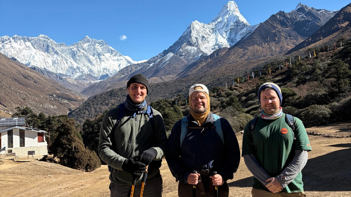 Three trekkers posing at Tengboche in December with Ama Dablam, Lhotse, and Mount Everest under a clear winter sky during the Everest Base Camp Trek