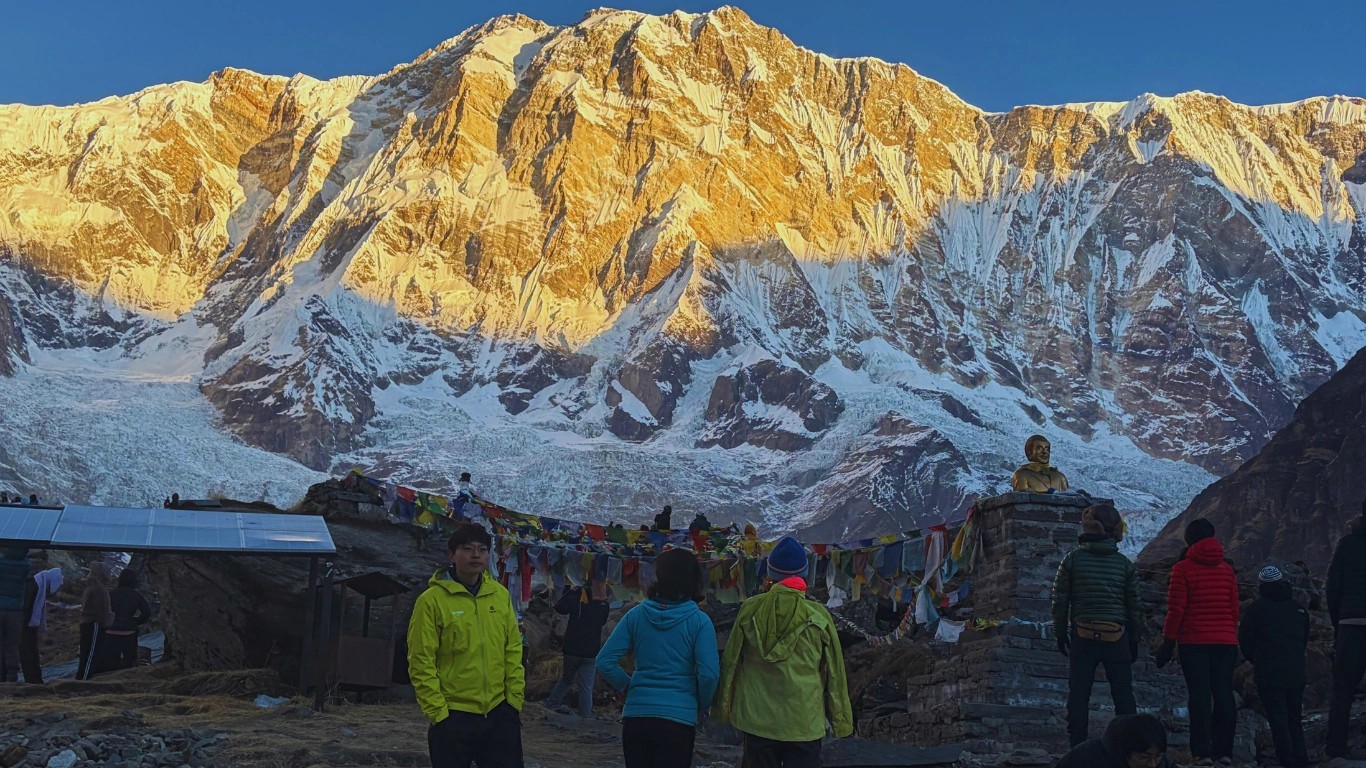 Guest watching morning sunrise on Annapurna I from Annapurna Base Camp viewpoint with glowing Himalayan peaks and dramatic high-altitude landscape.