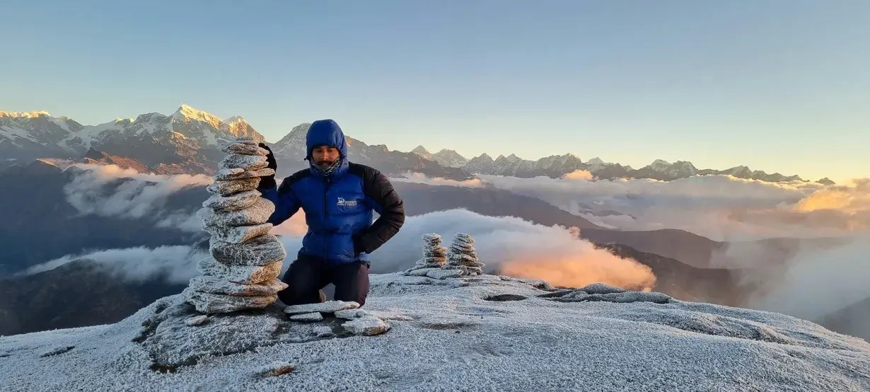 Trekking guide sitting in front of Pikey Peak viewpoint with light snow on the ground and mountain ranges in the background, Nepal.