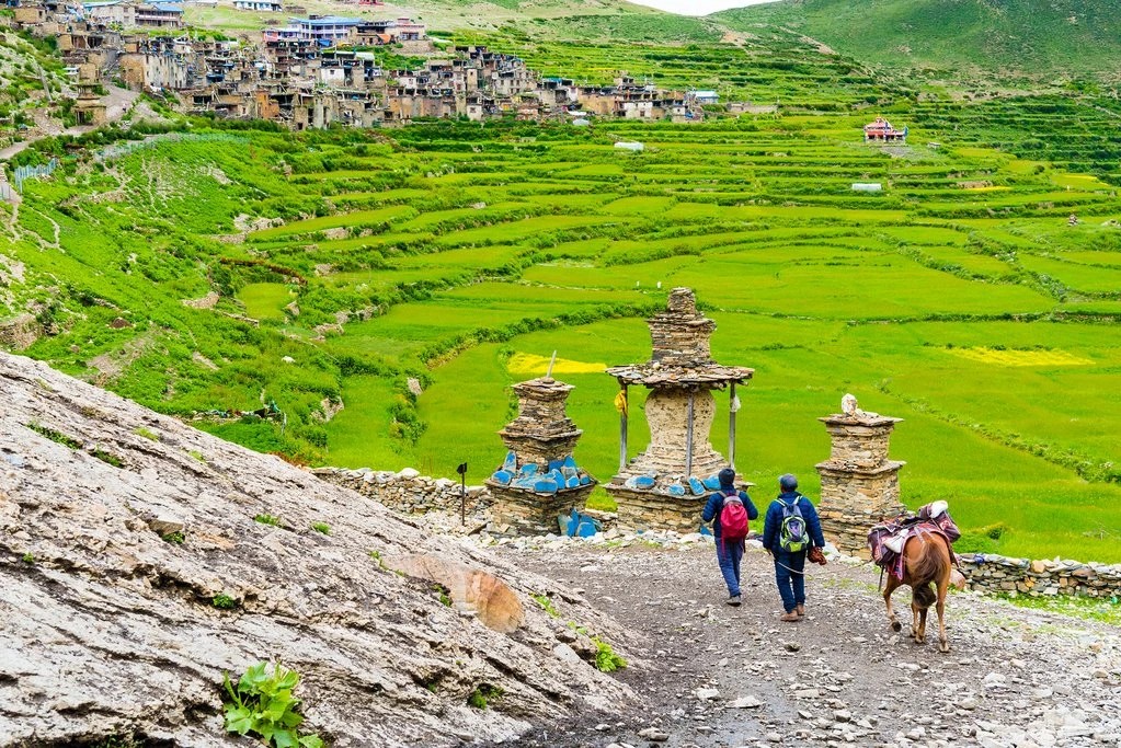 Trekkers walking into Nar Phu village during monsoon season with traditional stone houses and green valleys in Nepal