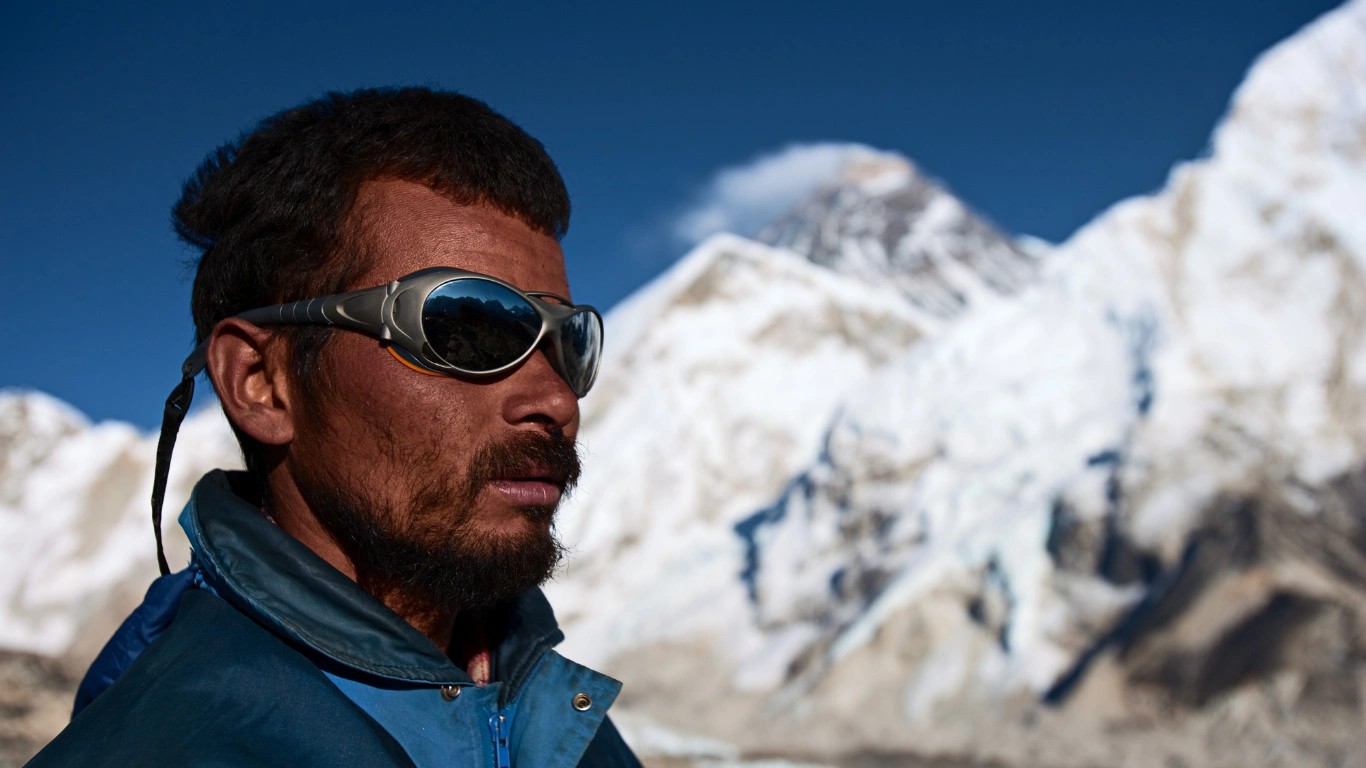 Sherpa mountaineer standing with Mount Everest rising behind him in the Khumbu region of Nepal.