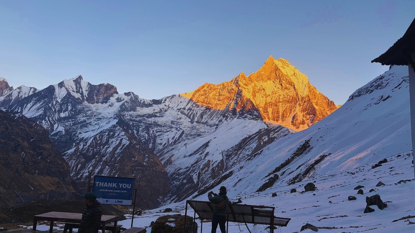 Trekkers taking photos of the golden sunset light on Machapuchare at Annapurna Base Camp.