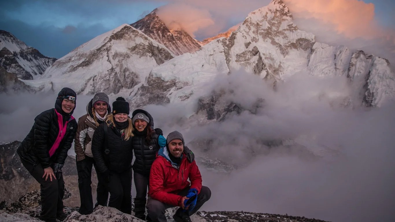 Group of trekkers standing at Kala Patthar viewpoint with Mount Everest glowing behind them during sunrise in the Everest region of Nepal.