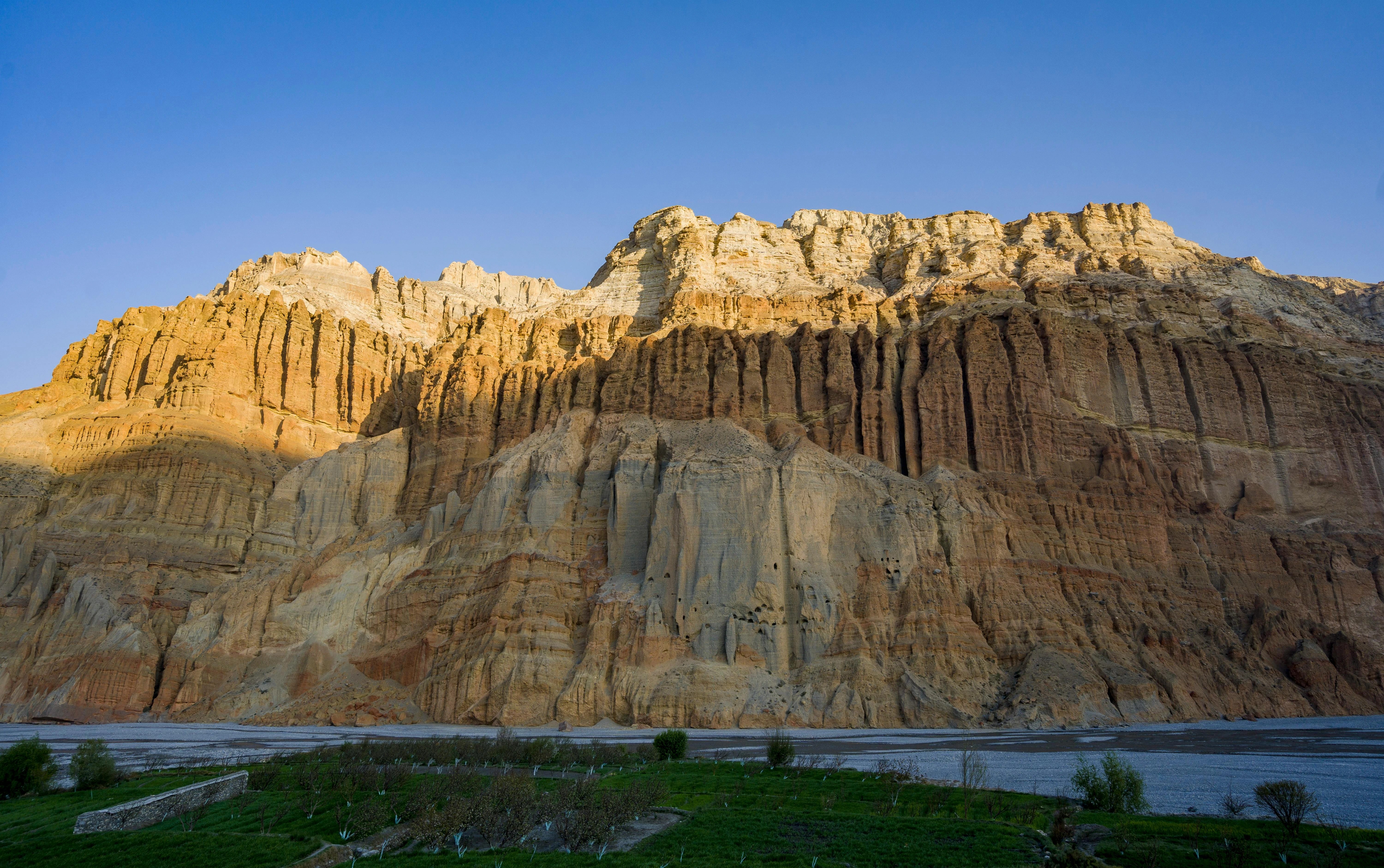 Traditional mud wall architecture in Upper Mustang Nepal with dry mountain landscape and blue sky in background.