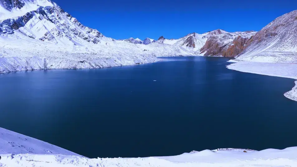 Crystal-clear Blue Tilicho Lake with surrounding snow-capped peaks in Annapurna region, Nepal, during a high-altitude lake trek.