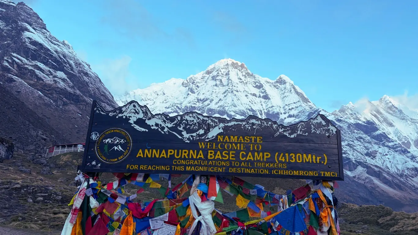 Annapurna Base Camp signboard at 4,130 meters with Annapurna South and snow-covered Himalayan peaks rising in the background.